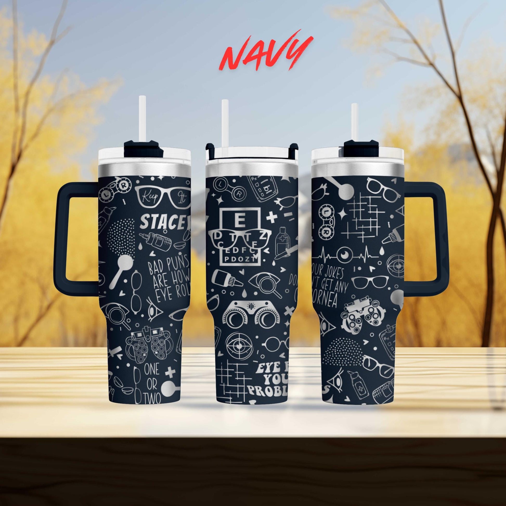 three black and white tumblers with various designs and text printed on them, placed on a wooden surface against a blurred background of trees.