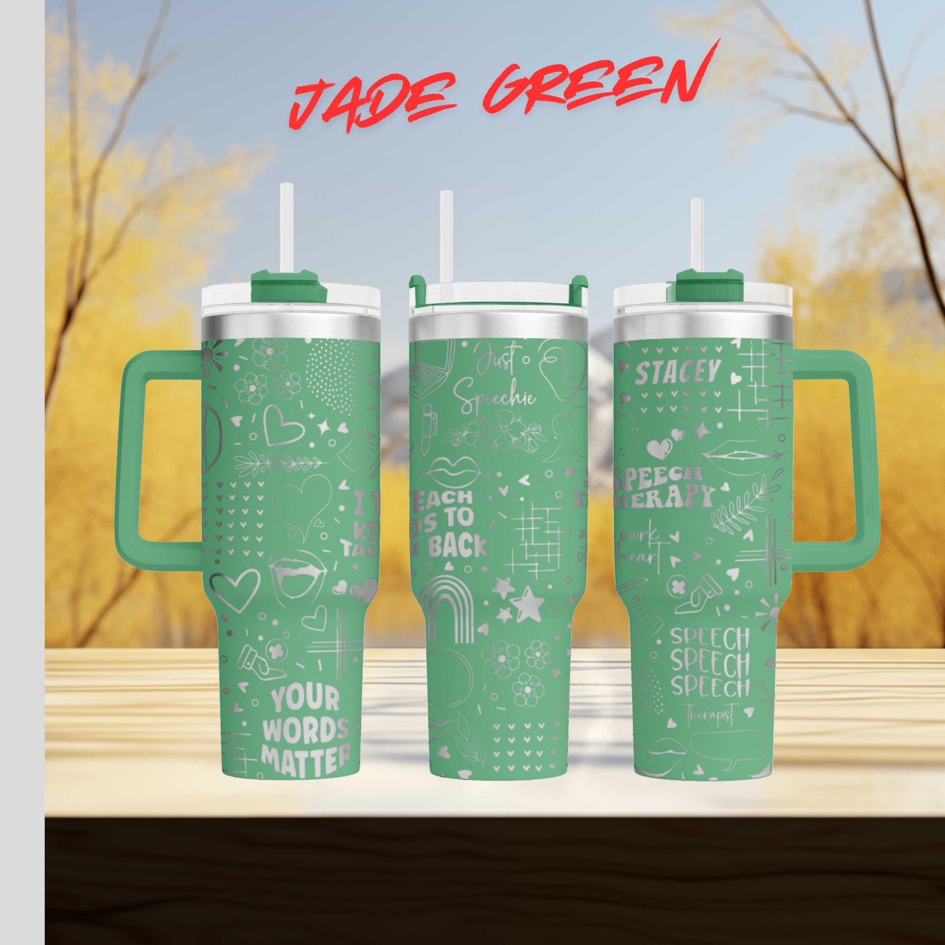 Three green tumblers with white text and designs on them, placed on a wooden surface against a blurred background of trees.