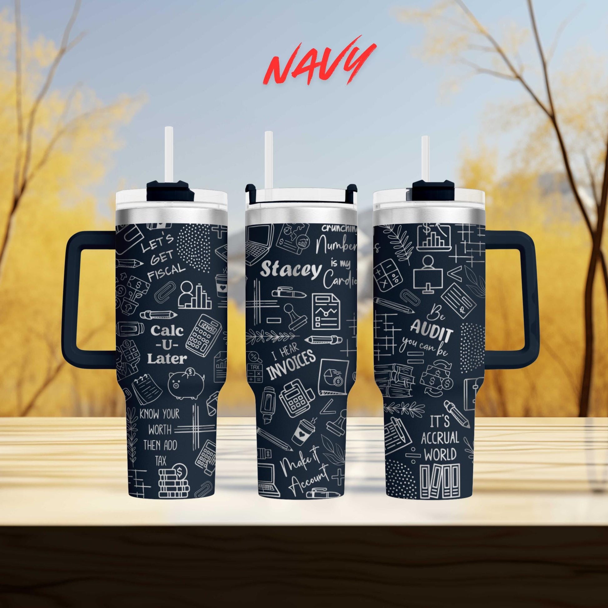 three black tumblers with white text and graphics printed on them, placed on a wooden surface against a blurred background of trees.