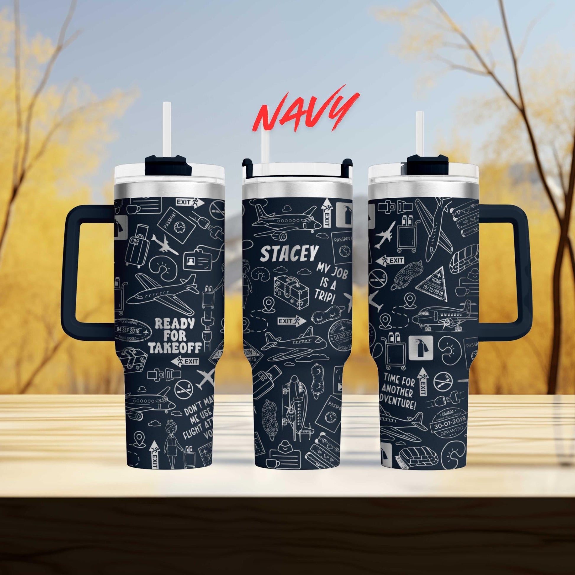 three black and white tumblers with various airplane and travel-related icons printed on them. The tumblers have handles and straws, and the background is blurred, suggesting a wooded area.