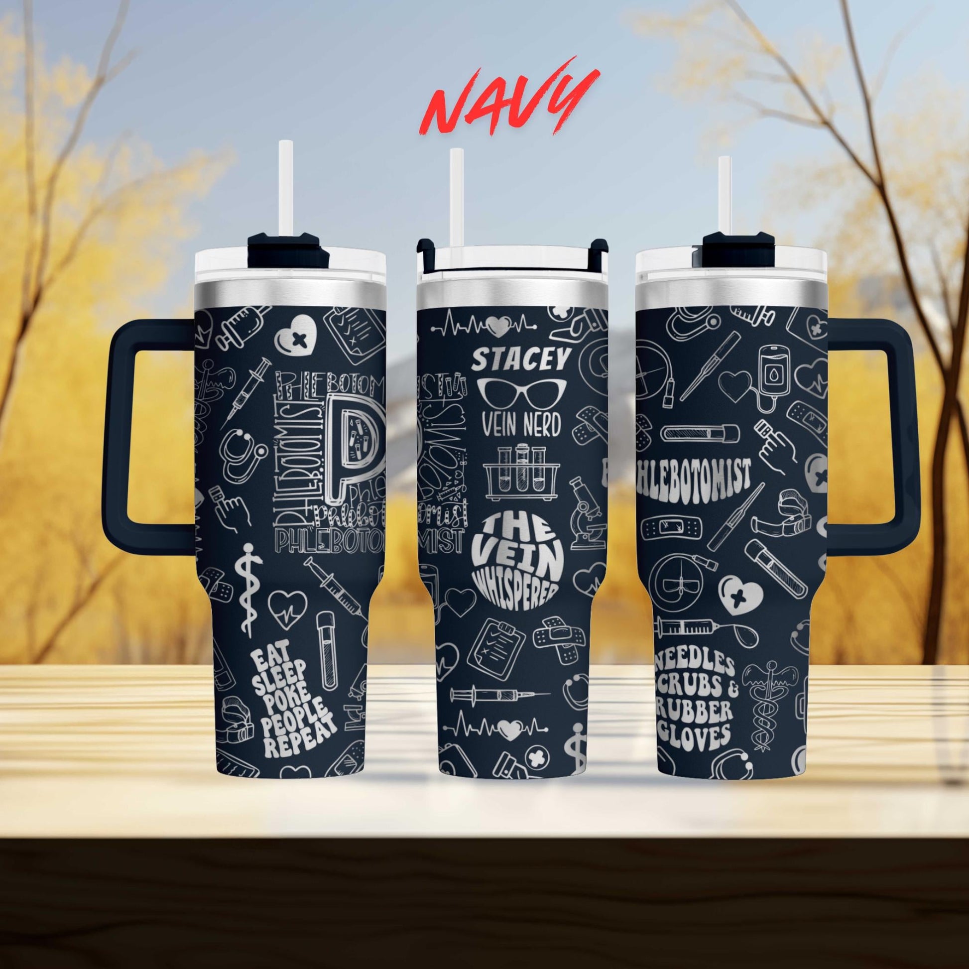 three black tumblers with white text and illustrations printed on them, set against a blurred background of trees.
