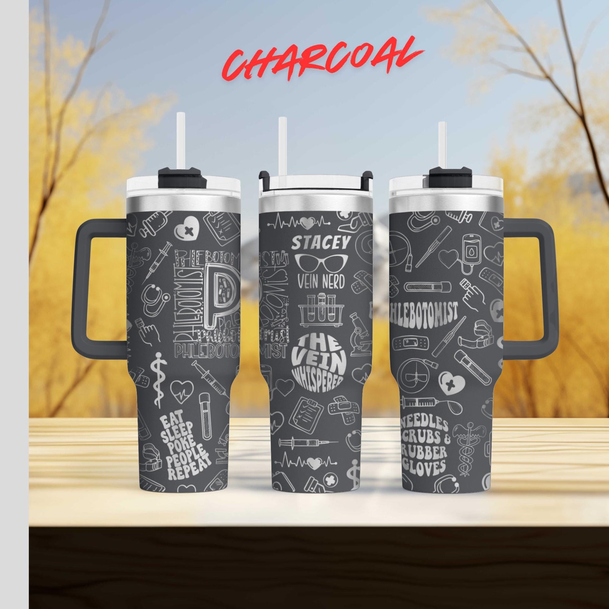 three black tumblers with white text and graphics printed on them, set against a blurred background of trees and sky.