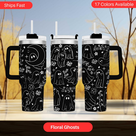 three black tumblers with a black and white ghost design printed on them. The tumblers are displayed on a wooden surface against a blurred background.