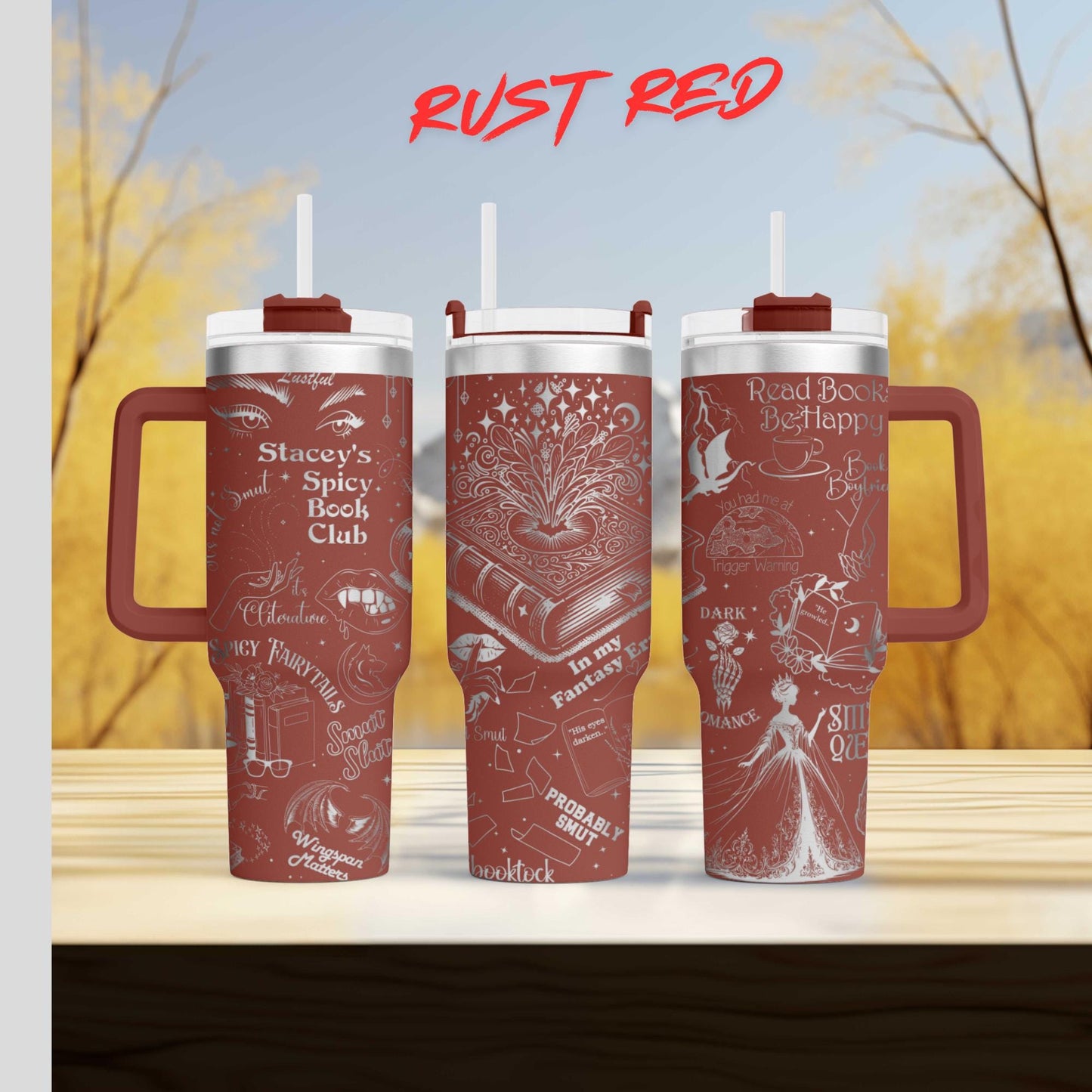 Three red tumblers with white text and illustrations on them, placed on a wooden surface against a blurred background of trees.
