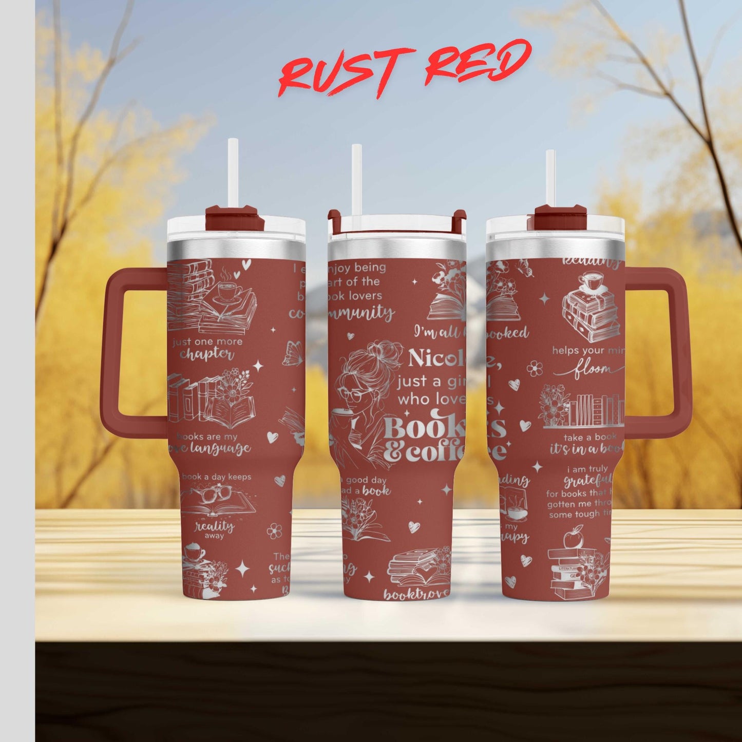Three red tumblers with white text and illustrations on them, placed on a wooden surface against a blurred background of trees.