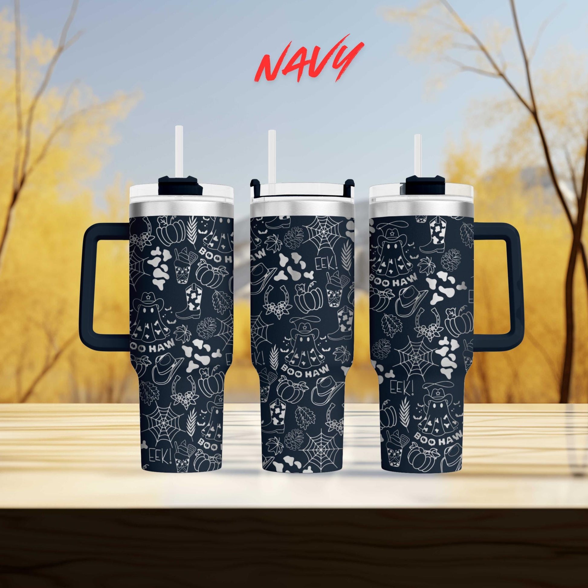 three black and white tumblers with a Halloween-themed design, including bats, pumpkins, and spiderwebs, displayed on a wooden surface against a blurred background of trees.