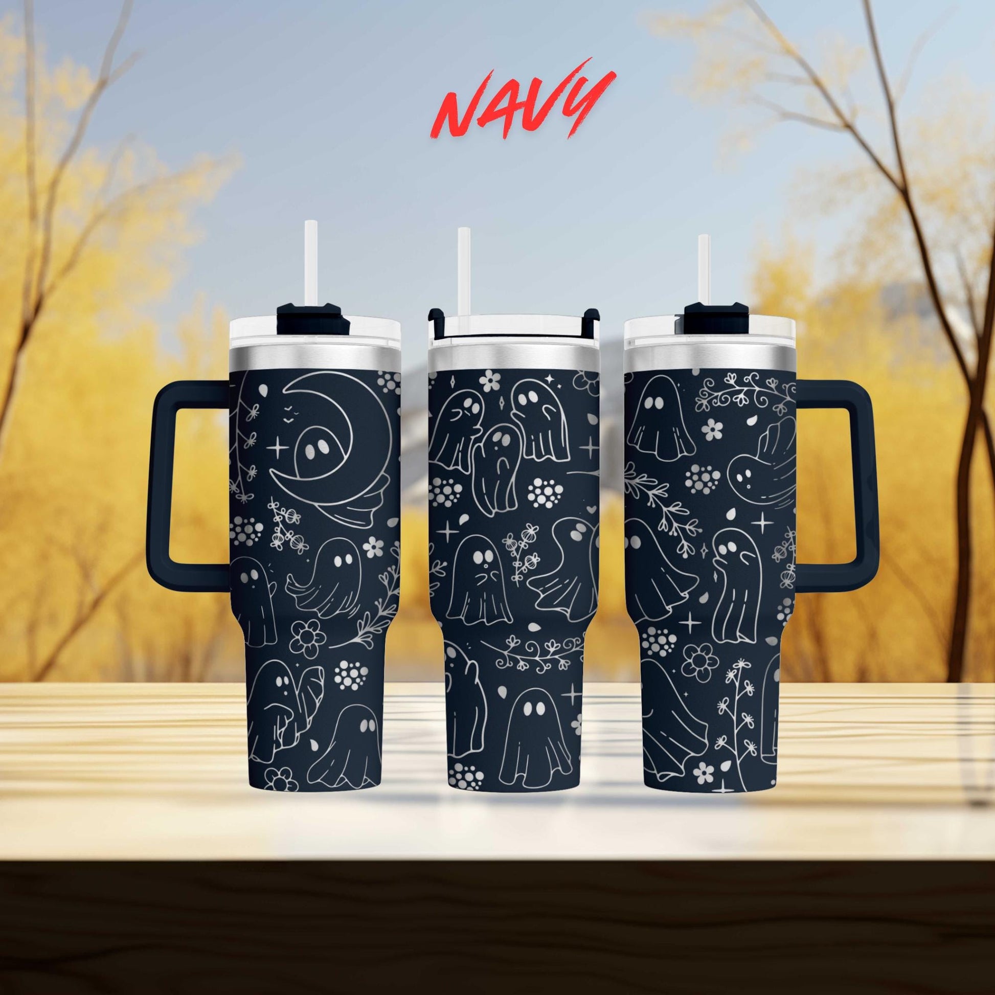 three black tumblers with a whimsical ghost and flower design printed on them, set against a blurred background of trees.