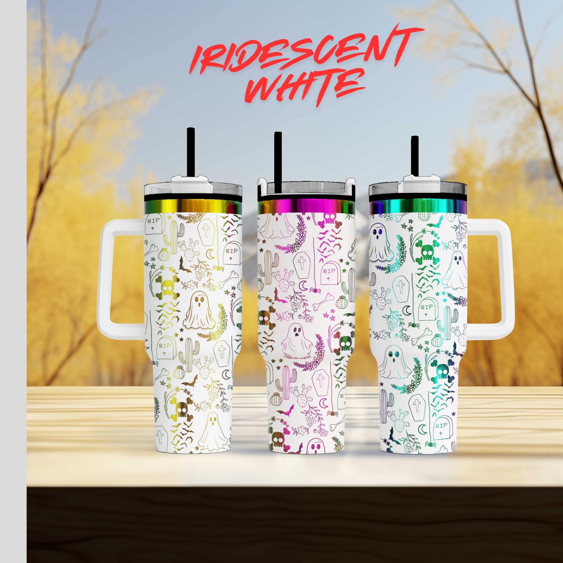 Three colorful tumblers with ghost and cactus designs, arranged on a wooden surface against a blurred background of trees.