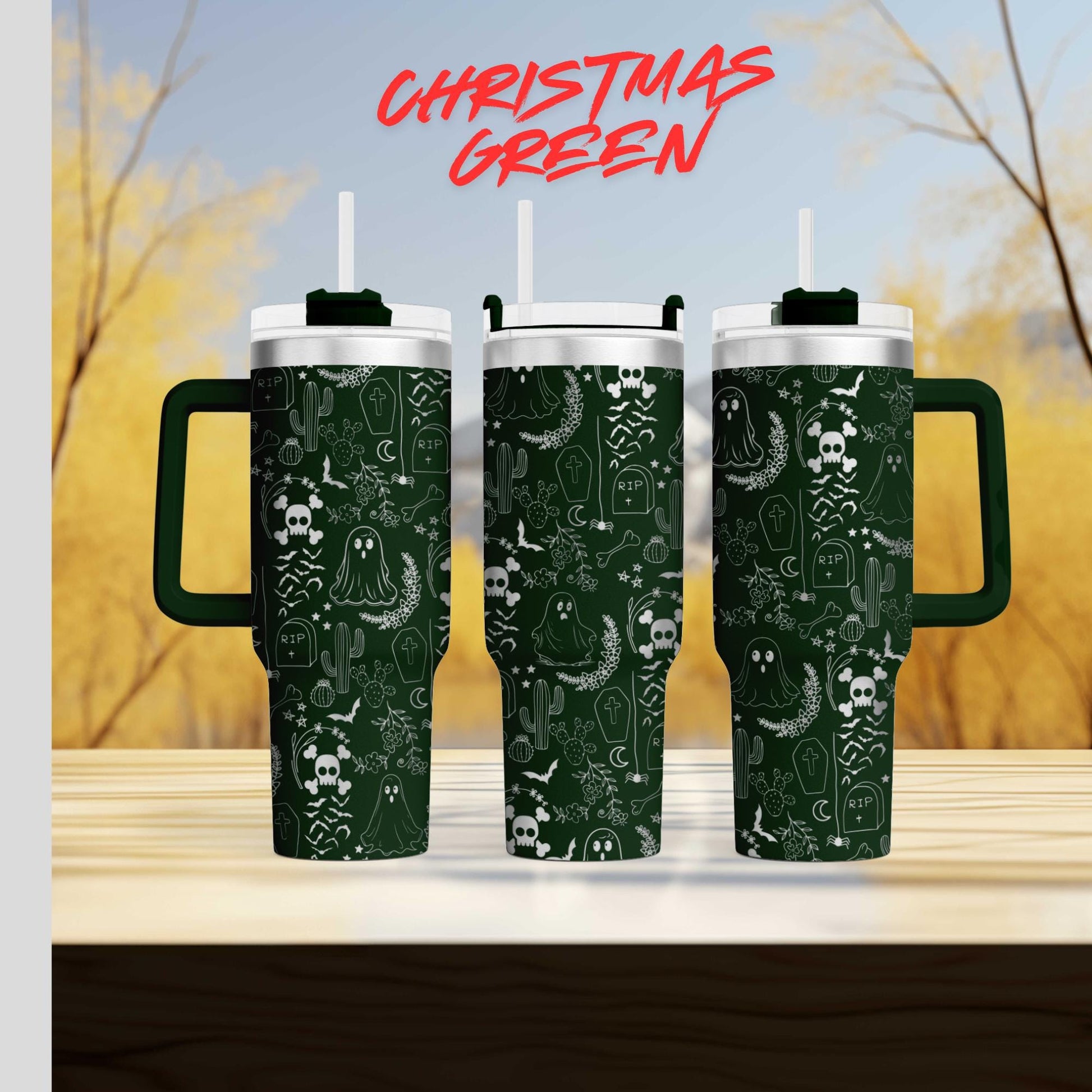 three green tumblers with a Halloween-themed design, including skulls, bats, and ghostly figures, against a blurred background of trees and sky.