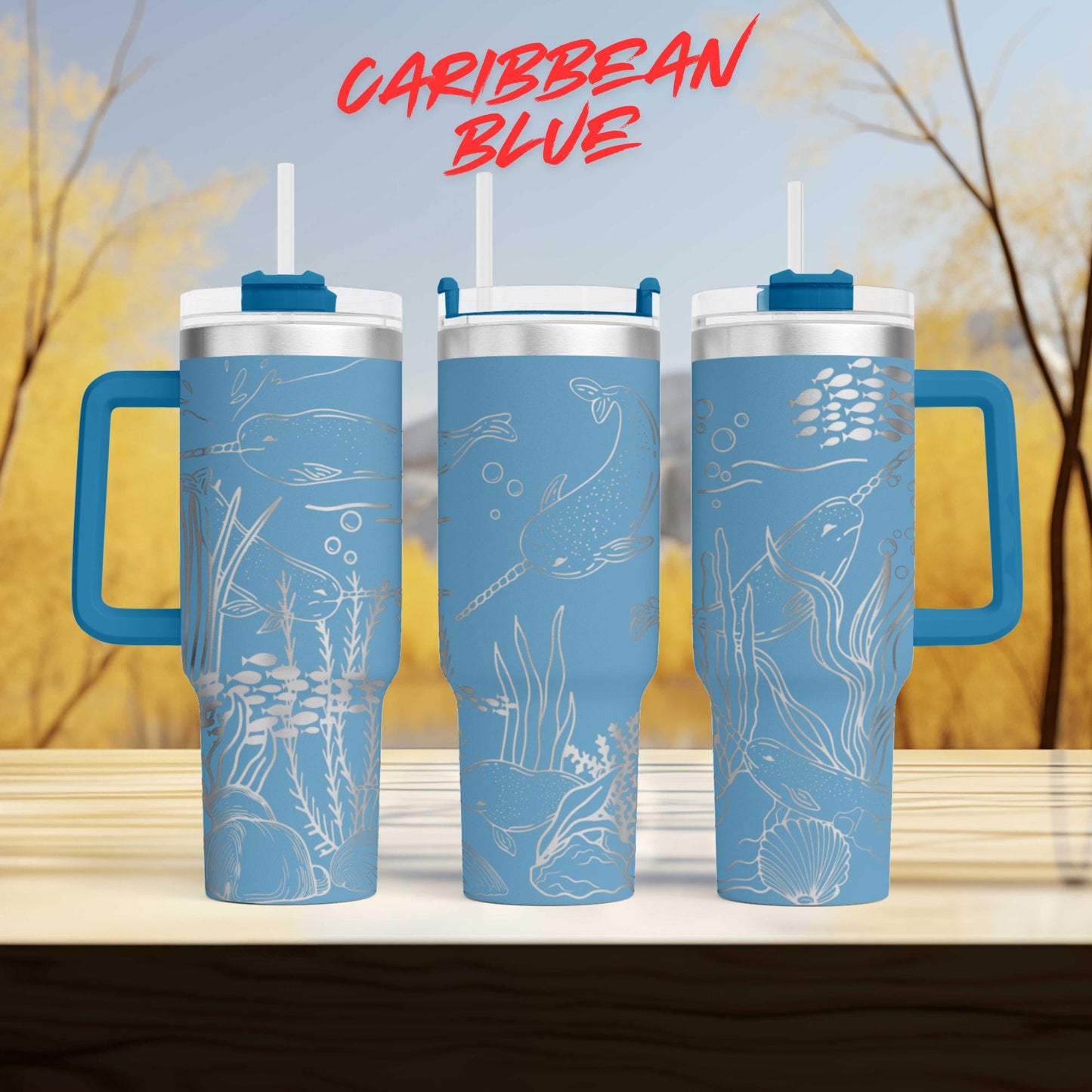 three blue tumblers with designs of marine life, including fish, plants, and other aquatic elements, against a blurred background of trees and sky.