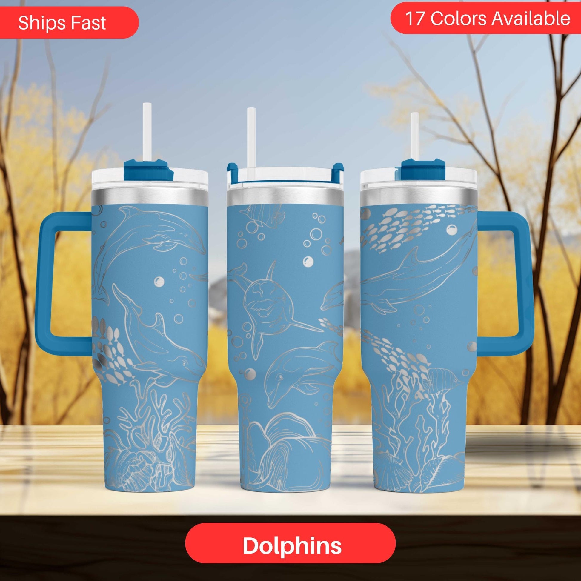 three blue tumblers with white dolphin designs, arranged in a row against a blurred background of trees.