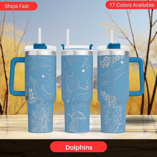 three blue tumblers with white dolphin designs, arranged in a row against a blurred background of trees.