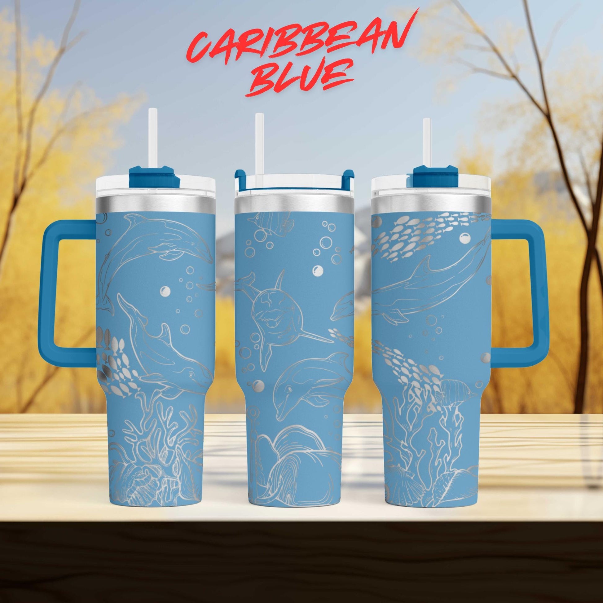 three blue tumblers with designs of marine life, including dolphins and bubbles, against a blurred background of trees.