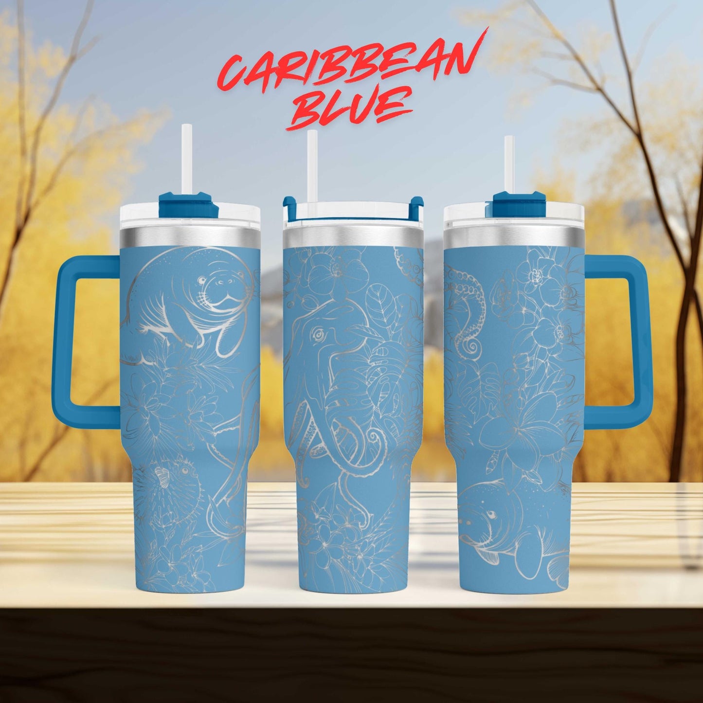three blue tumblers with handles, each adorned with a unique design, set against a blurred background of trees.