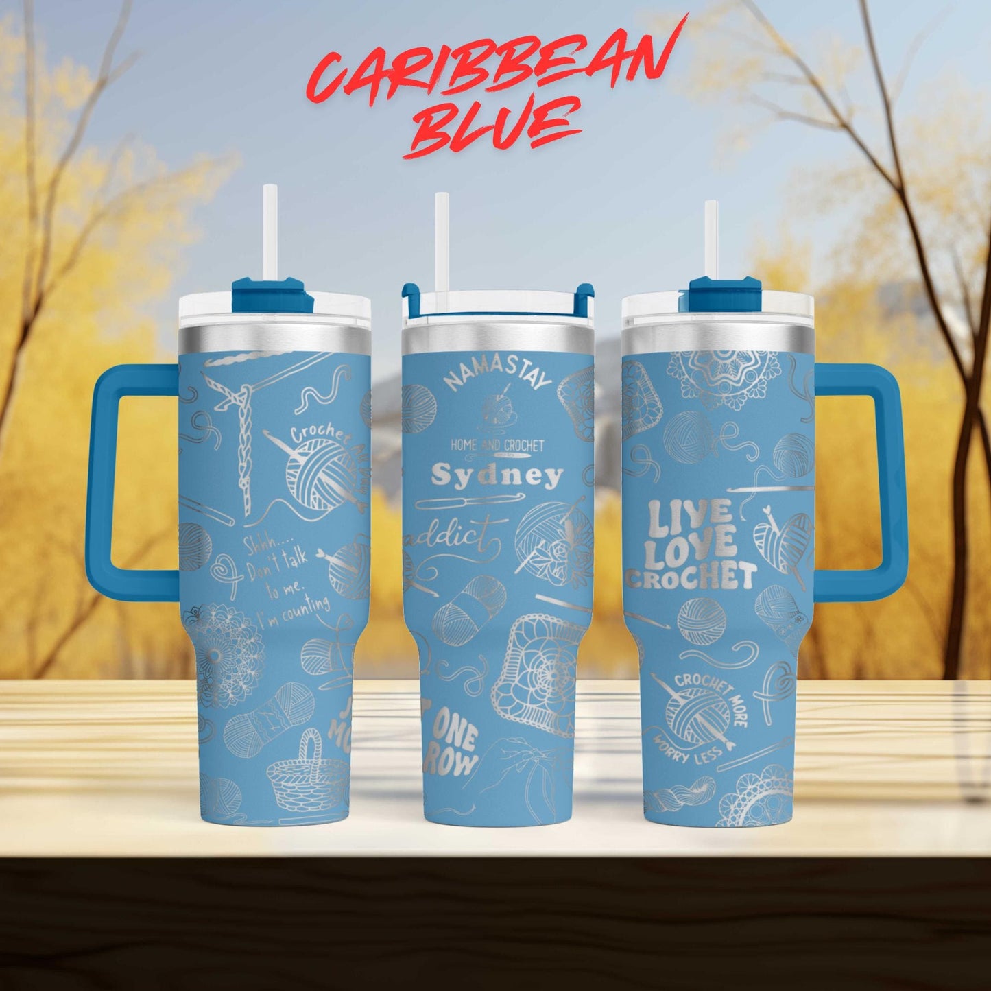three blue tumblers with various designs and text on them, set against a blurred background of trees and a blue sky.