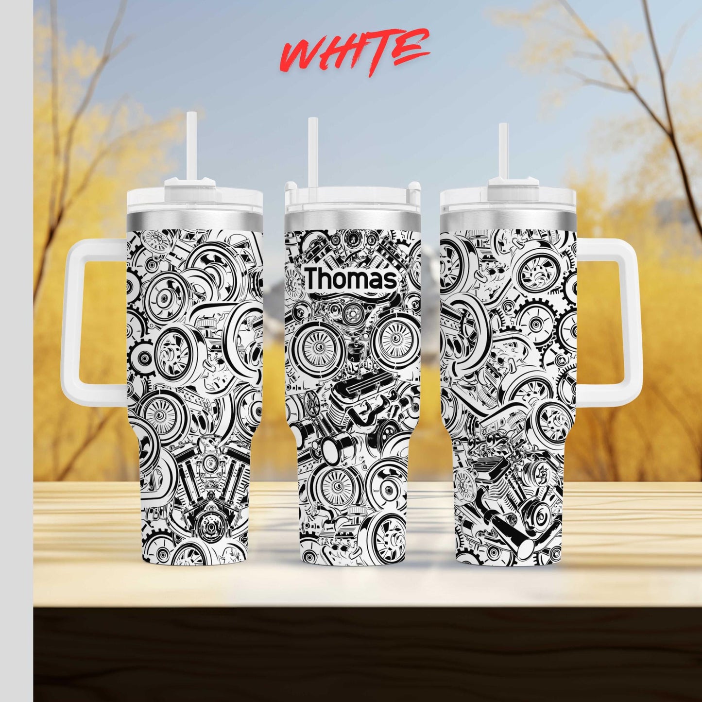 three black and white tumblers with the name "Thomas" printed on them. The tumblers are placed on a wooden surface against a blurred background of trees and foliage.