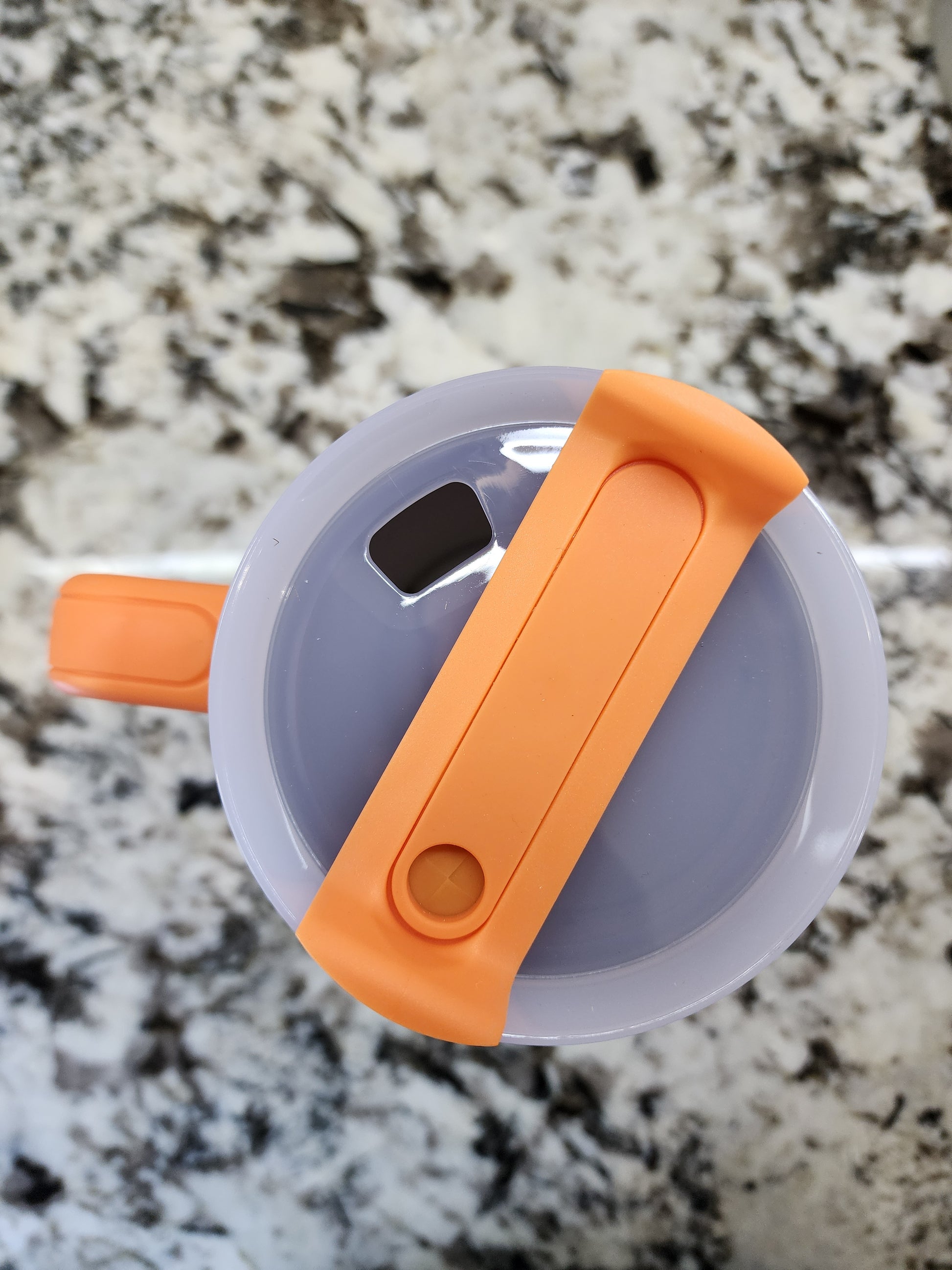 a plastic cup with an orange handle on a marble surface