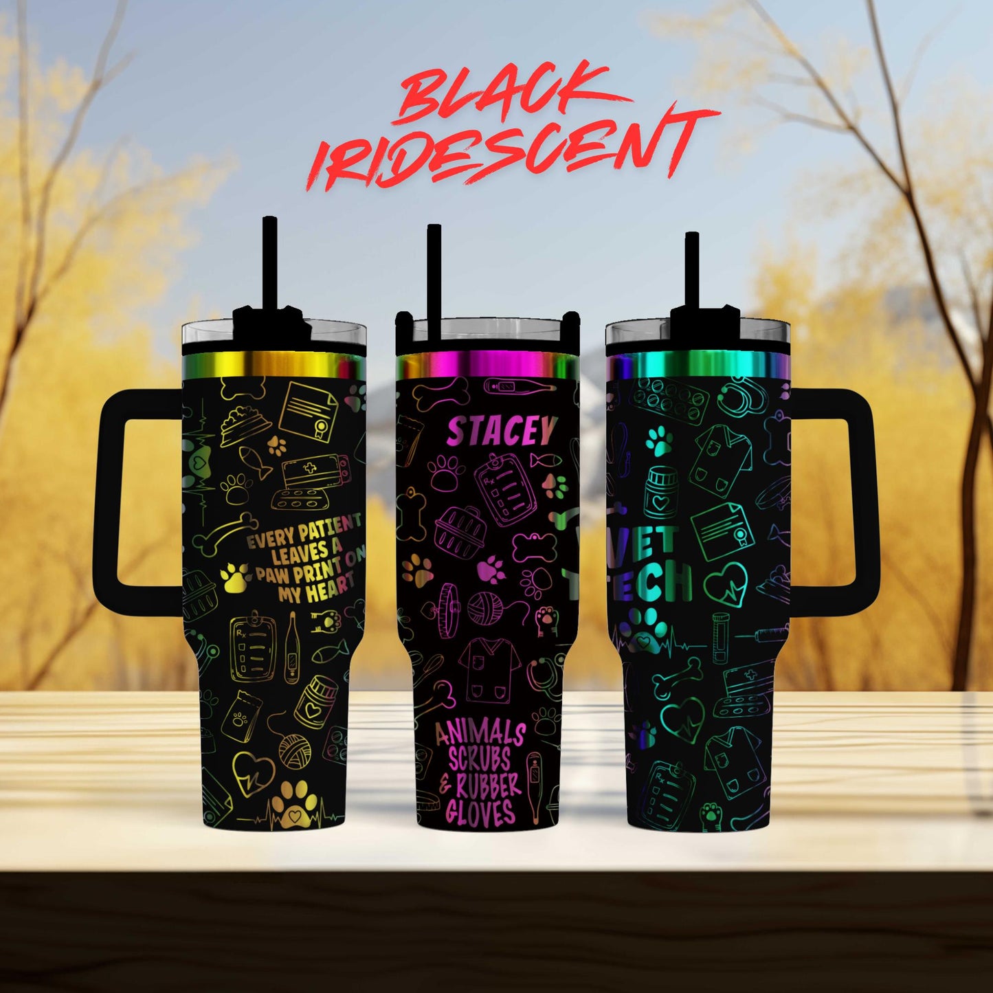 three colorful tumblers with various designs and text on them, placed on a wooden surface against a blurred background of trees.
