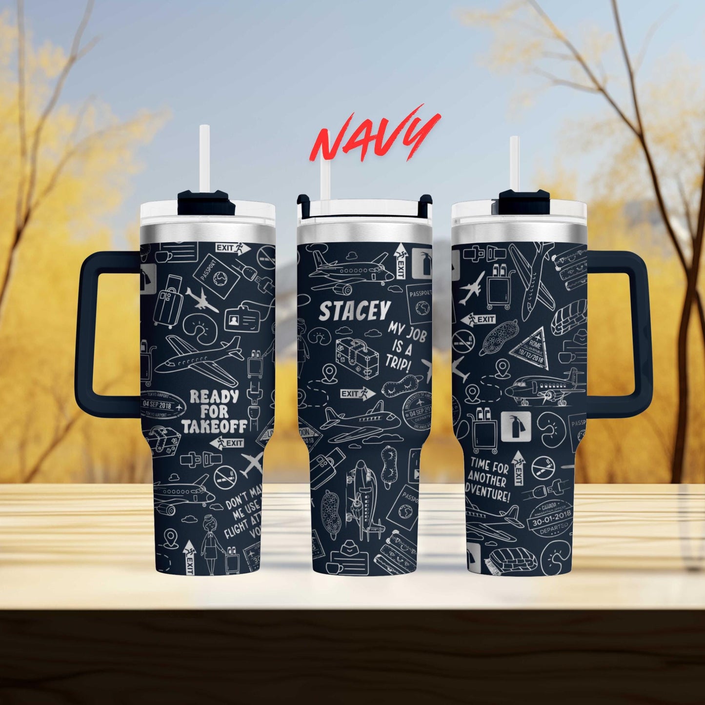 three black and white tumblers with various airplane and travel-related icons printed on them. The tumblers have handles and straws, and the background is blurred, suggesting a wooded area.