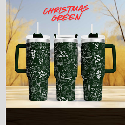 three green tumblers with white designs, including various Halloween-themed elements such as bats, pumpkins, and spiders, against a blurred background of trees and a blue sky.