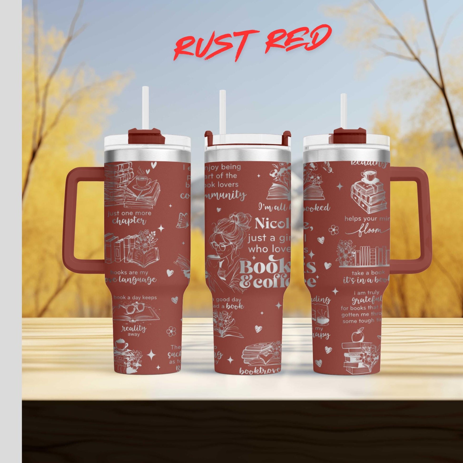 Three red tumblers with white text and illustrations on them, placed on a wooden surface against a blurred background of trees.