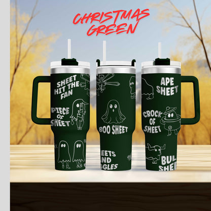 three green tumblers with white text and illustrations on them, set against a blurred background of trees and sky.