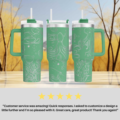 three green tumblers with white designs, including an octopus and bubbles, placed on a wooden surface against a blurred background of trees.