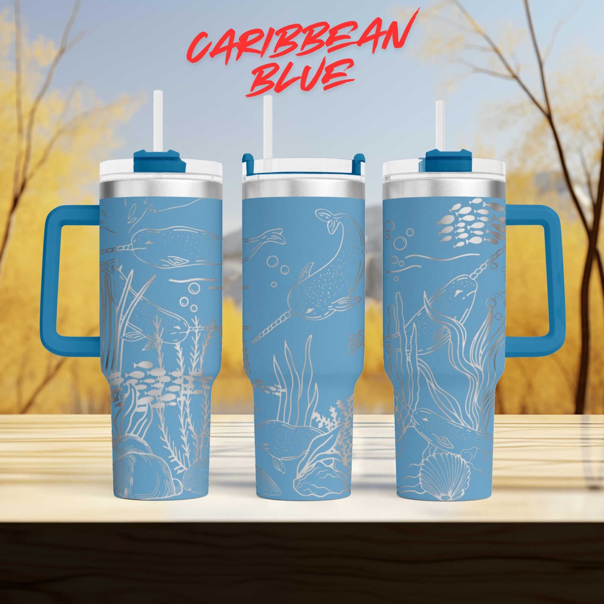 three blue tumblers with designs of marine life, including fish, plants, and other aquatic elements, against a blurred background of trees and sky.