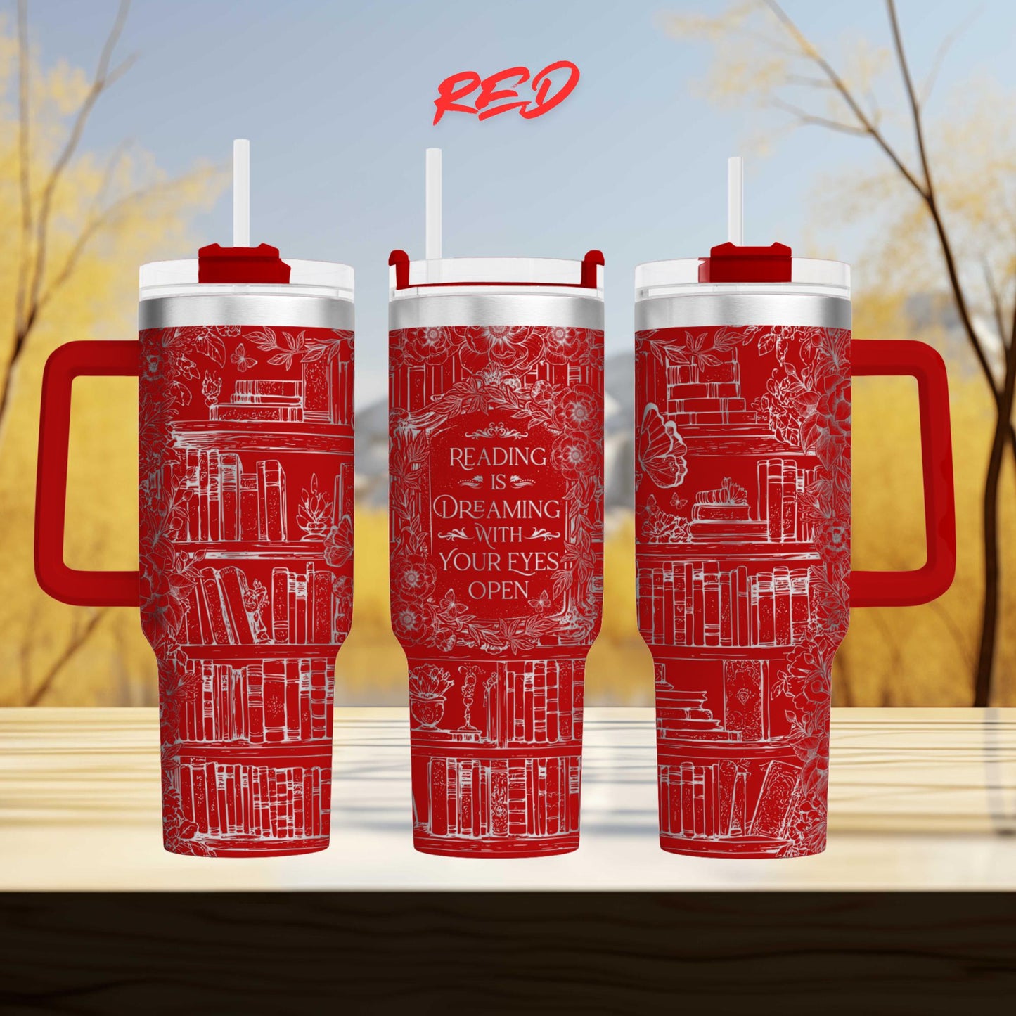 three red insulated tumblers with white text and illustrations on them, set against a blurred background of trees.