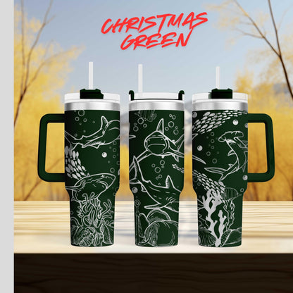 three green tumblers with white designs depicting marine life, such as sharks and coral, against a blurred background of trees and sky.