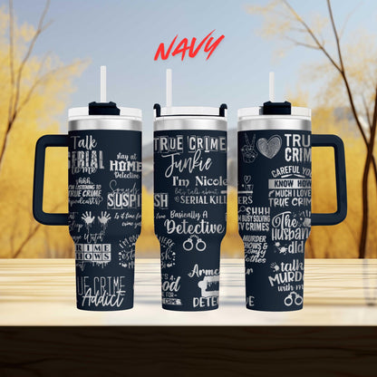 three black tumblers with white text and phrases printed on them, placed on a wooden surface against a blurred background.