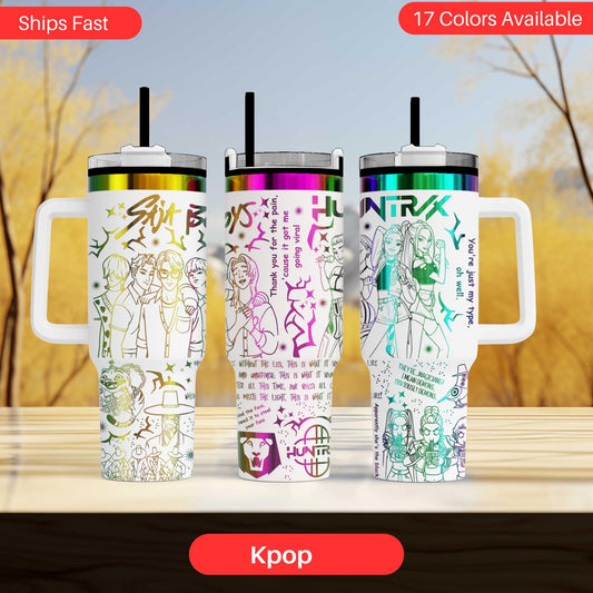 Three colorful tumblers with various designs and text, including Korean text, are displayed on a wooden surface against a blurred background.