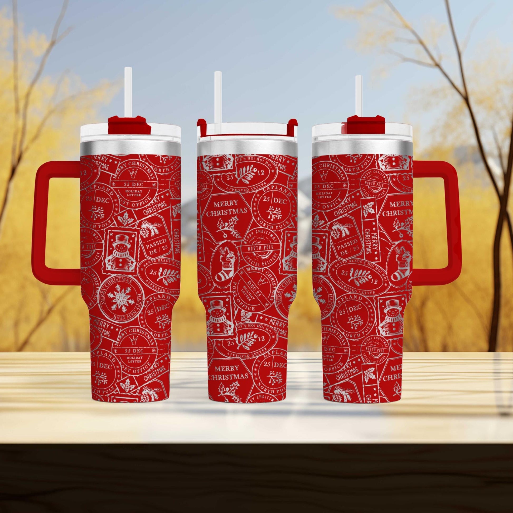 Three red and white patterned thermos tumblers with handles, arranged on a wooden surface against a blurred background of trees.